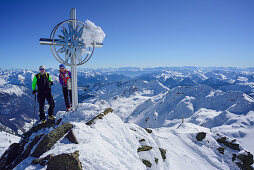 Man and woman back-country skiing standing at the cross on the summit of Schneespitze, Schneespitze, valley of Pflersch, Stubai Alps, South Tyrol, Italy