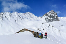 Drei Personen auf Skitour stehen vor Almhütte, Tete dell' Autaret und Pelvo di Ciabriera im Hintergrund, Monte Faraut, Valle Varaita, Cottische Alpen, Piemont, Italien