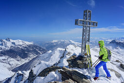 Woman back-country skiing standing at cross at summit of Monte Salza, Monte Salza, Valle Varaita, Cottian Alps, Piedmont, Italy