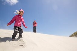 A girl in a sandstorm on the dunes of Wharariki Beach, Farewell Spit, South Island, New Zealand