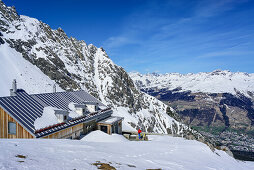 Frau auf Skitour steht vor Hütte Chamanna Lischana, Piz Lischana, Sesvennagruppe, Engadin, Graubünden, Schweiz