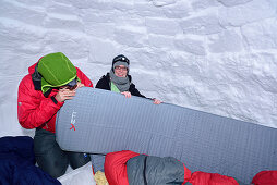 Zwei Personen sitzen in Iglu und blasen Luftmatratze auf, Chiemgauer Alpen, Chiemgau, Oberbayern, Bayern, Deutschland