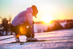 Young woman tying her shoes before cross-country skiing at sunset, Allgaeu, Bavaria, Germany