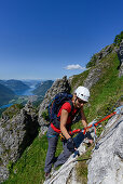 Woman climbing the Via ferrata del Centenario in front of Lake Lugano and the highest Swiss mountain, the snow-capped Dufourspitze (4634 m) in the Monte Rosa massif, Italy and Switzerland