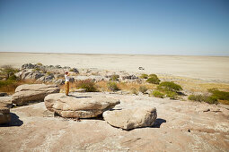 Frau steht auf Felsblock und schaut über Salzwüste, Kubu Island, Makgadikgadi Pans Nationalpark, Botswana