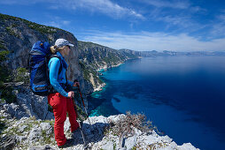 A young woman with trekking gear standing at the mountainous coast above the sea, Golfo di Orosei, Selvaggio Blu, Sardinia, Italy, Europe