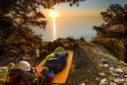 Young woman sleeping in her sleeping bag at sunrise near the bay Cala Biriola, Trekking- and climbing gear visible, Golfo di Orosei, Selvaggio Blu, Sardinia, Italy, Europe