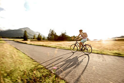 Junge Frau fährt mit ihrem Fahrrad bei einer Wiese an einem sonnigen Tag, Tannheimer Tal, Tirol, Österreich
