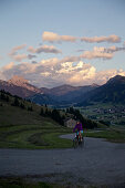 Junge Frau fährt mit ihrem Fahrad in der Nähe der Berge bei Sonnenuntergang, Rote Flüh, Gimpel, Hochwiesler, Tannheimer Tal, Tirol, Österreich