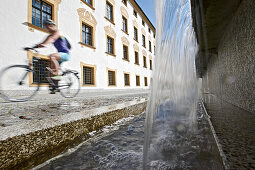 Young female cyclist riding past a fountain, Kempten, Bavaria, Germany