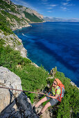 Frau seilt über Felswand ab, Mittelmeer im Hintergrund, Selvaggio Blu, Nationalpark Golfo di Orosei e del Gennargentu, Sardinien, Italien