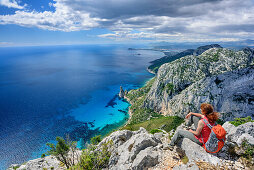 Frau beim Wandern sitzt an Punta Giradili und blickt auf Golfo di Orosei mit Felsnadel Pedra Longa, Selvaggio Blu, Nationalpark Golfo di Orosei e del Gennargentu, Sardinien, Italien