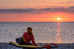 Woman laying in sleeping bag at beach and looking at sunrise, Selvaggio Blu, National Park of the Bay of Orosei and Gennargentu, Sardinia, Italy