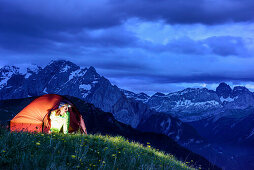 Woman sitting in illuminated tent, Marmolada in background, Sella range, UNESCO world heritage Dolomites, Dolomites, Trentino, Italy