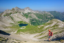 Woman hiking descending towards lake Hintersee, Stanskogel and Fallesinspitze in background, Lechtal Alps, Tyrol, Austria