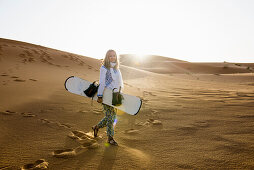 junge Frau mit Snowboard in den Sanddünen bei Merzouga, Erg Chebbi, Sahara, Marokko, Afrika