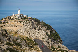 Young couple riding a red Vespa scooter on road along Cap de Formentor peninsula with Faro de Formentor lighthouse behind, Palma, Mallorca, Balearic Islands, Spain