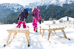 Mädchen und Junge ziehen ihre Holzschlitten, Pfronten, Allgäu, Bayern, Deutschland