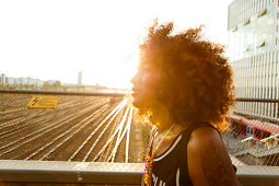 Young afro-american woman in backlight in urban scenery with tracks and station, Hackerbruecke Munich, Bavaria, Germany