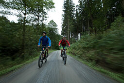 Cyclists riding down a path through a forest
