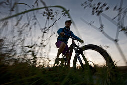 Junge Frau fährt Fahrrad auf einem Weg zwischen Feldern