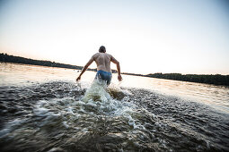 Young man running into the water of a lake, Freilassing, Bavaria, Germany