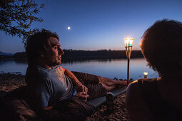 Young man lying at a lake at night, Freilassing, Bavaria, Germany