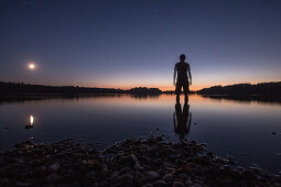 Young man standing in a lake at night, Freilassing, Bavaria, Germany