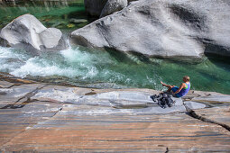 Young female hiker sitting on a rock at a river, Valle Verzasca, Ticino, Switzerland