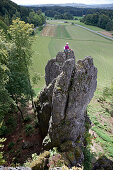 Young female climber sitting on the top of a high rock, Pottenstein, Franconia, Germany