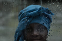 Einheimisches junges Mädchen steht hinter einem regenbedecktem Fenster, Sao Tome, Sao Tome und Príncipe, Afrika