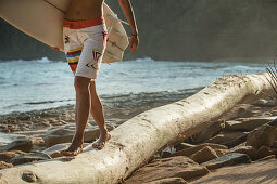 Junge Surferin balanciert über einen Baumstamm am Strand, Sao Tome, Sao Tome und Príncipe, Afrika