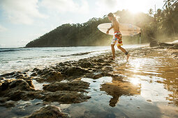 Young female surfer walking along the beach, Sao Tome, Sao Tome and Principe, Africa