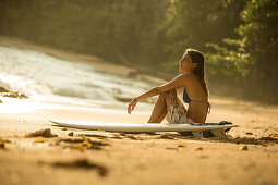 Junge Surferin sitzt am Strand mit ihrem Surfbrett, Sao Tome, Sao Tome und Príncipe, Afrika