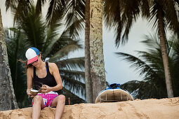 Young female surfer sitting in the sand and eating a coconut, Sao Tome, Sao Tome and Principe, Africa