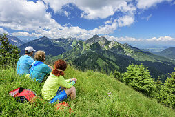 Three persons hiking sitting in meadow and looking to ridge of Klammspitze, Hennenkopf, Ammergau Alps, Upper Bavaria, Bavaria, Germany