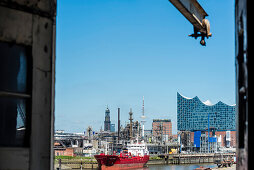 Blick aus einem Lagerhaus auf Industrieanlagen im Hamburger Hafen mit der Elbphilharmonie, dem Michel und dem Fernsehturm im Hintergrund, Hamburg, Deutschland
