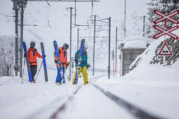 Three young male skiers going over railroad tracks, Andermatt, Uri, Switzerland