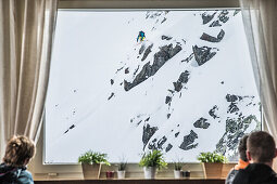 Gäste beobachten einen Skifahrer bei einem Sprung durchs Fenster, Andermatt, Uri, Schweiz