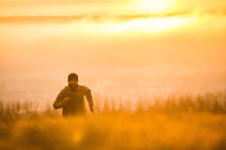 Young man running over a meadow during sunset, Allgaeu, Bavaria, Germany