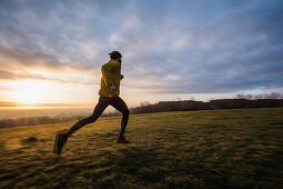 Young man running over a meadow during sunrise, Allgaeu, Bavaria, Germany