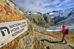 Woman hiking descending from pass Birnluecke, signpost of National Park Hohe Tauern in foreground, pass Birnluecke, National Park Hohe Tauern, Dreilaendertour, Zillertal Alps, South Tyrol, Italy