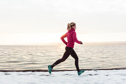 young woman running along the snowy Lake Starnberg, Bavaria, Germany.
