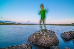 lachendes Kind steht auf einem Stein im See im Abendlicht wie ein Schemen, See nähe Munkfors, Värmland, Schweden
