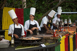 Fröhliche Köchinnen und Köche beim Beach Barbecue Abendessen am Strand vom Half Moon Resort, Rose Hall, nahe Montego Bay, Saint James, Jamaika
