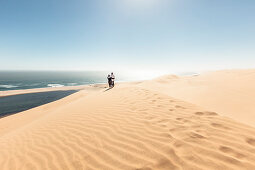 A couple in the dunes high above the lagoons of Sandwich Harbour, Walvis Bay, Erongo, Namibia, Africa