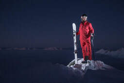 Junger Skifahrer steht auf dem Gipfel eines Berges über den Wolken bei Nacht, Kaprun, Salzburg, Österreich
