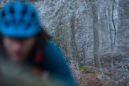 Young man riding with his bike through a with frost covered forest, Allgaeu, Bavaria, Germany