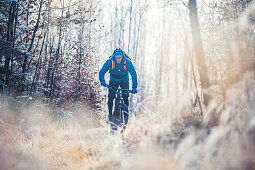 Young man riding with his bike through a with frost covered forest, Allgaeu, Bavaria, Germany