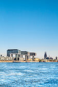 View over river Rhein towards Rheinau harbour with crane houses, Cologne Cathedral, Cologne, North Rhine-Westphalia, Germany